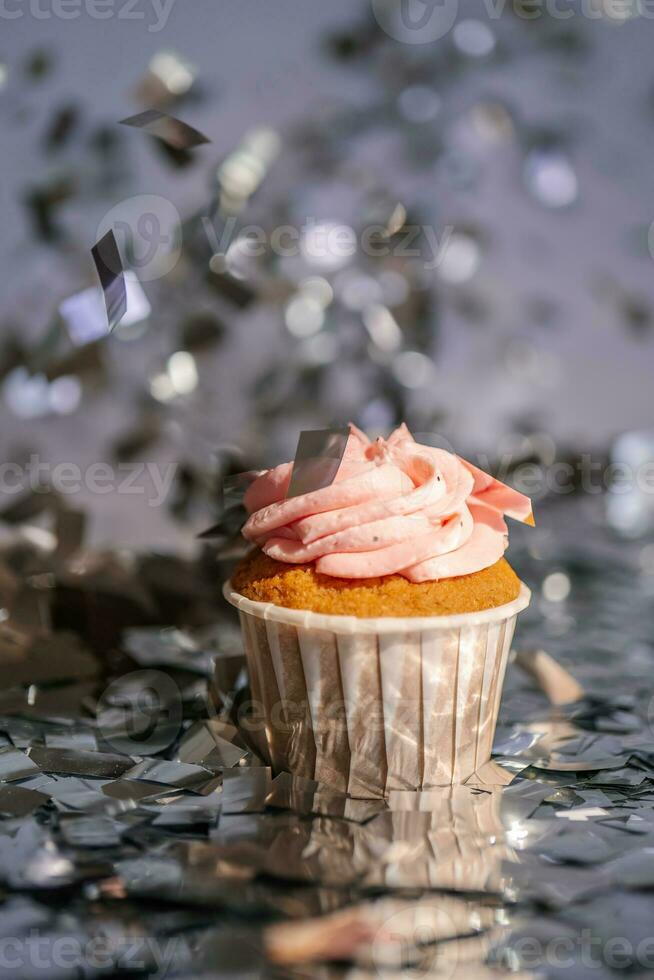 en muffin med en rosa keps står bland de flygande silver- konfetti. foto