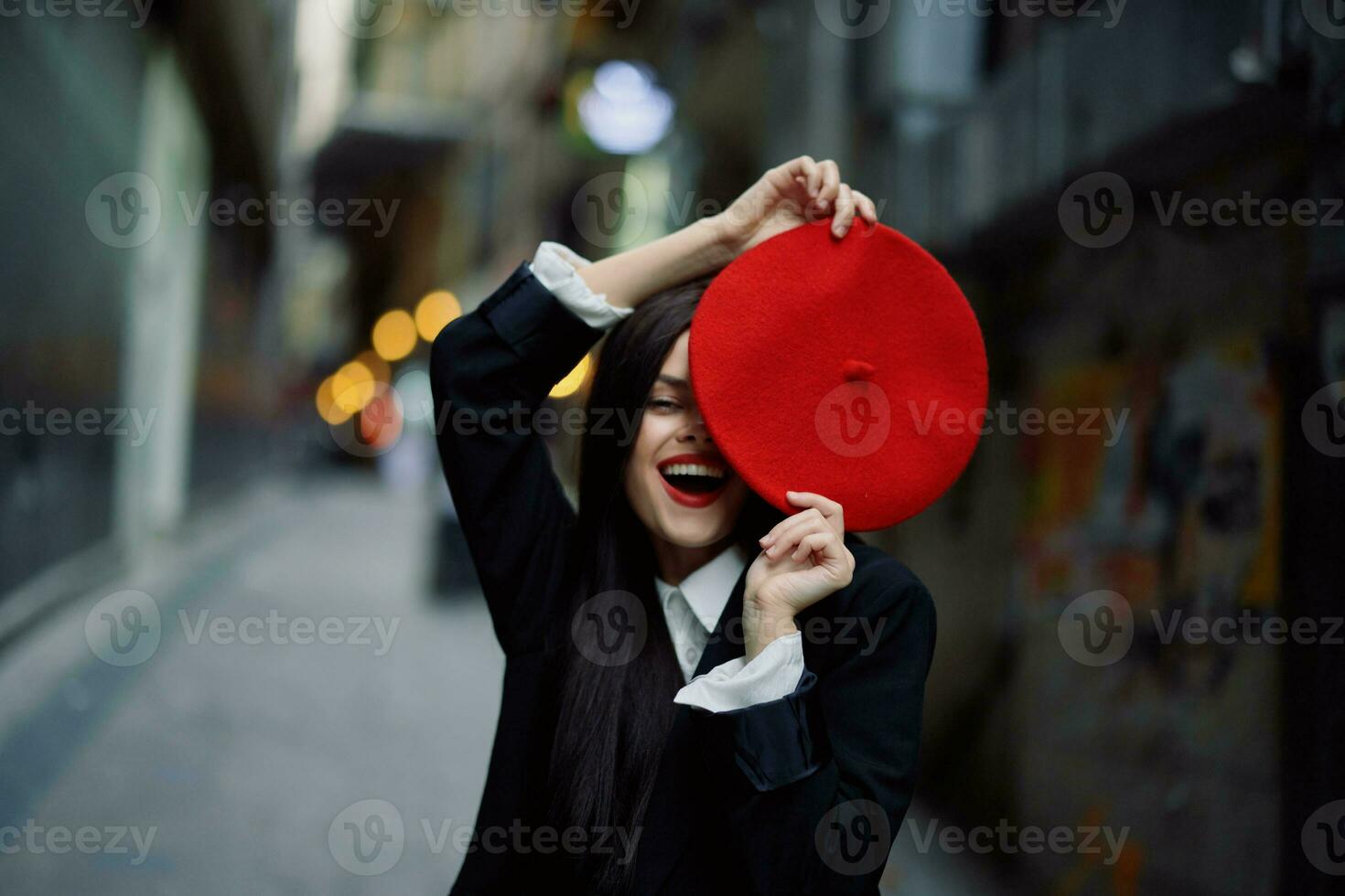 mode kvinna leende med tänder och roligt turist i eleganta kläder i jacka och röd basker gående ner smal stad gata flygande hår, resa, franska stil, filmiska Färg, retro stil. foto