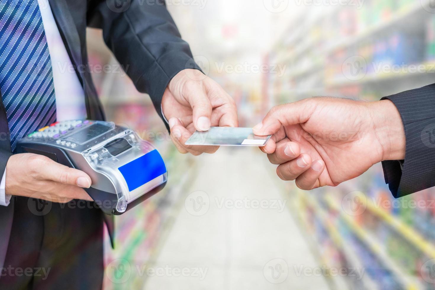 hand som håller betalkreditkort med affärsmannen som använder betalningsterminalen på stormarknadaffär foto