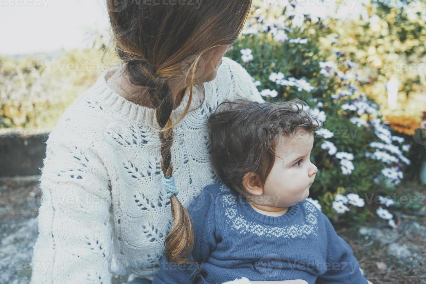 ung mamma kramar sitt barn och njuter av en vårdag i trädgården foto