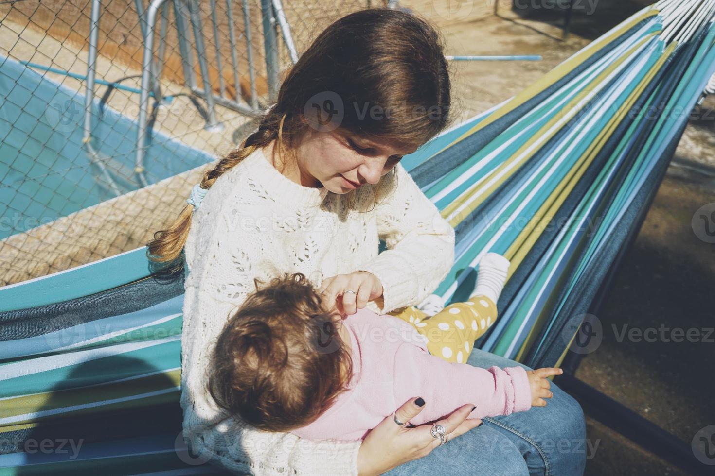 ung kvinna som bryr sig sitt barn sitter på en hängmatta foto