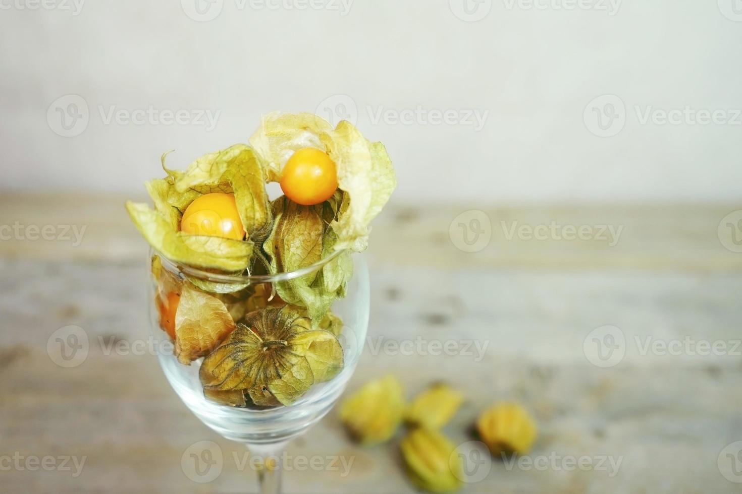 vacker och elegant makro närbild av mycket orange välsmakande frukt med namnet physalis från Peru, Sydamerika, i ett kristallglas med utrymme över träbord foto