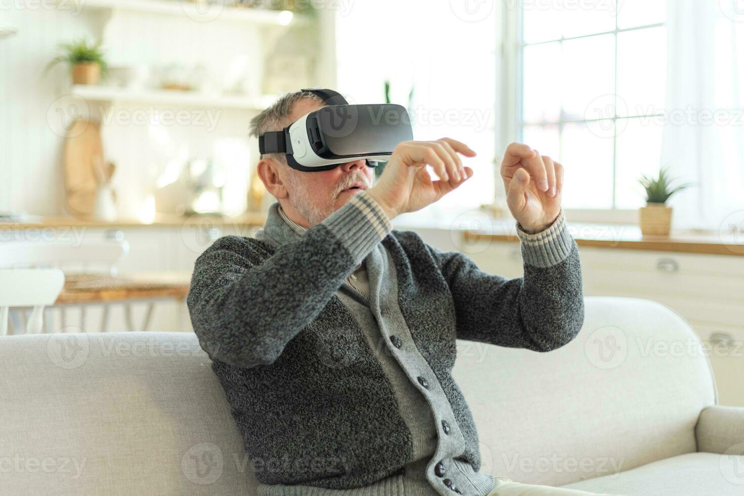 upphetsad mogna senior man bär använder sig av virtuell verklighet metavers vr glasögon headsetet på Hem. farfar rörande luft under vr erfarenhet på virtuell verklighet hjälm. simulering hi-tech TV-spel. foto