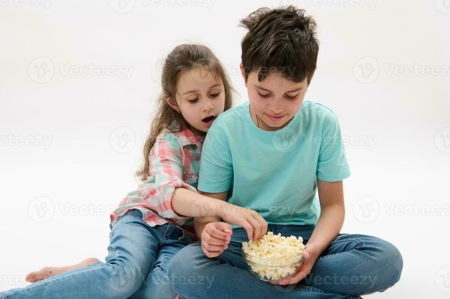 skön barn - Tonårs pojke och preschooler flicka äter gott saltade popcorn, isolerat över vit studio bakgrund foto