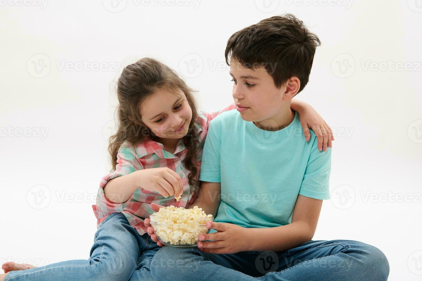 härlig liten flicka kramas henne äldre bror medan tittar på film eller tecknade serier, Sammanträde tillsammans på vit bakgrund foto