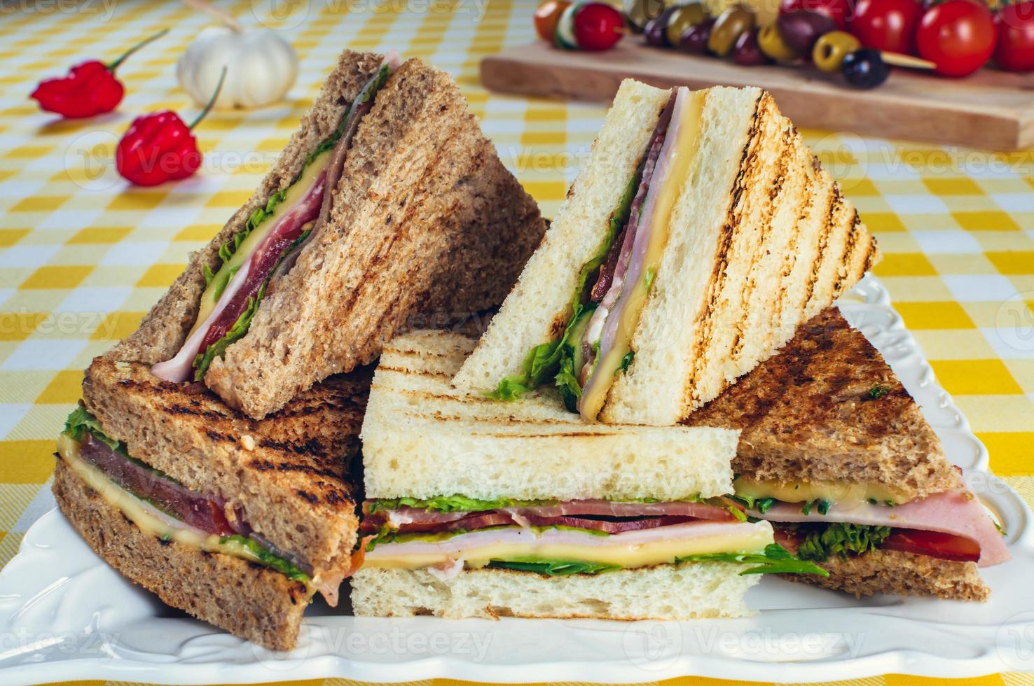 klubbsmörgås med skinka, salami, rökt nötkött, ost, sallad och rucola. rostat brödsmack. foto