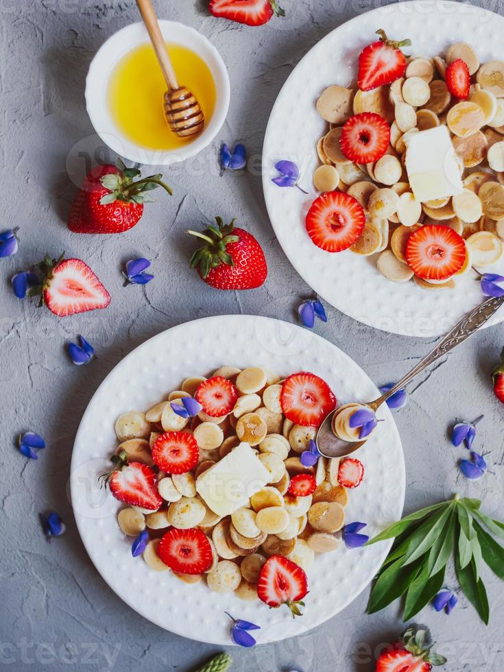 pannkakaflingor, trendig mat. mini spannmålspannkakor med smör, honung och jordgubbar. foto