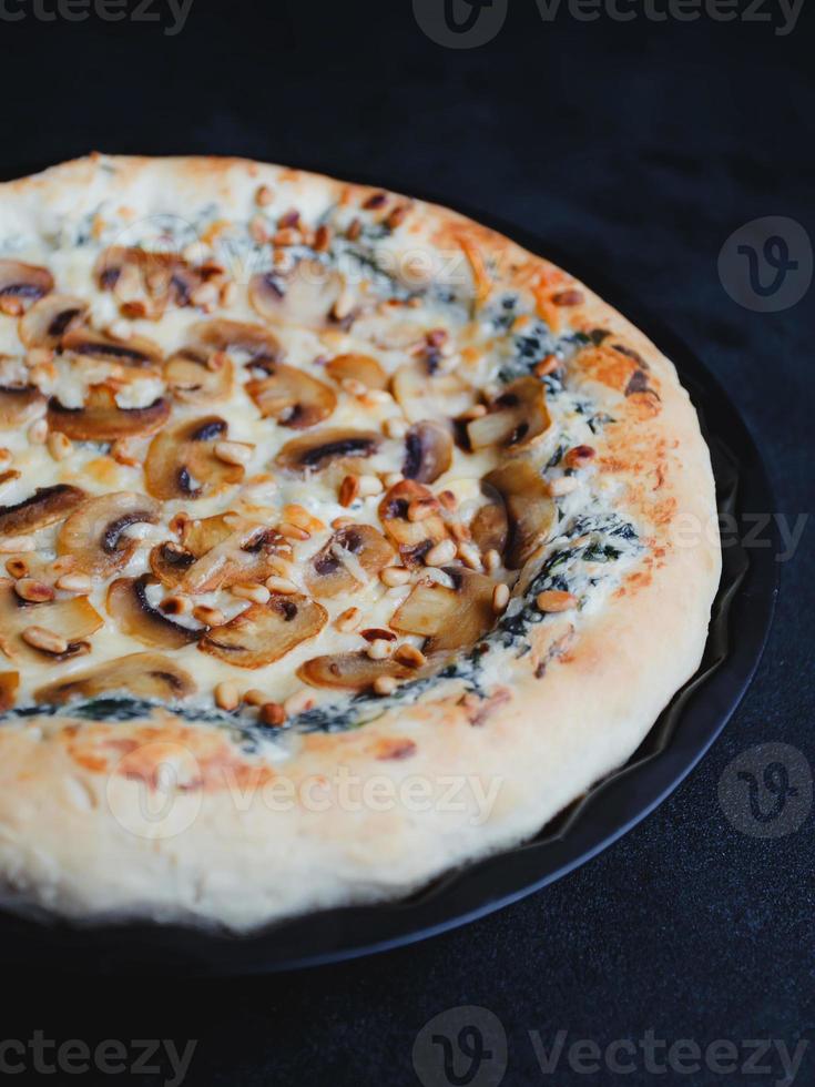 hemlagad pizza med svamp, spenat, vitlök, gräddeost och pinjenötter, på en mörk bakgrund. foto