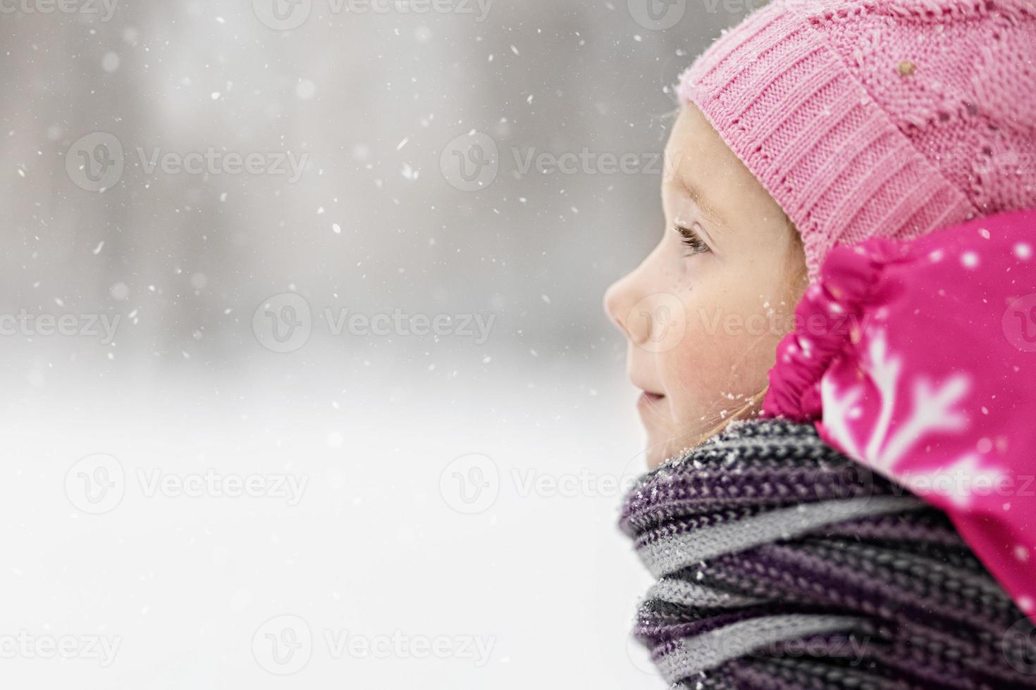 porträtt av en liten flicka i rosa närbild. ett barn njuter av snöfallet. jullov foto