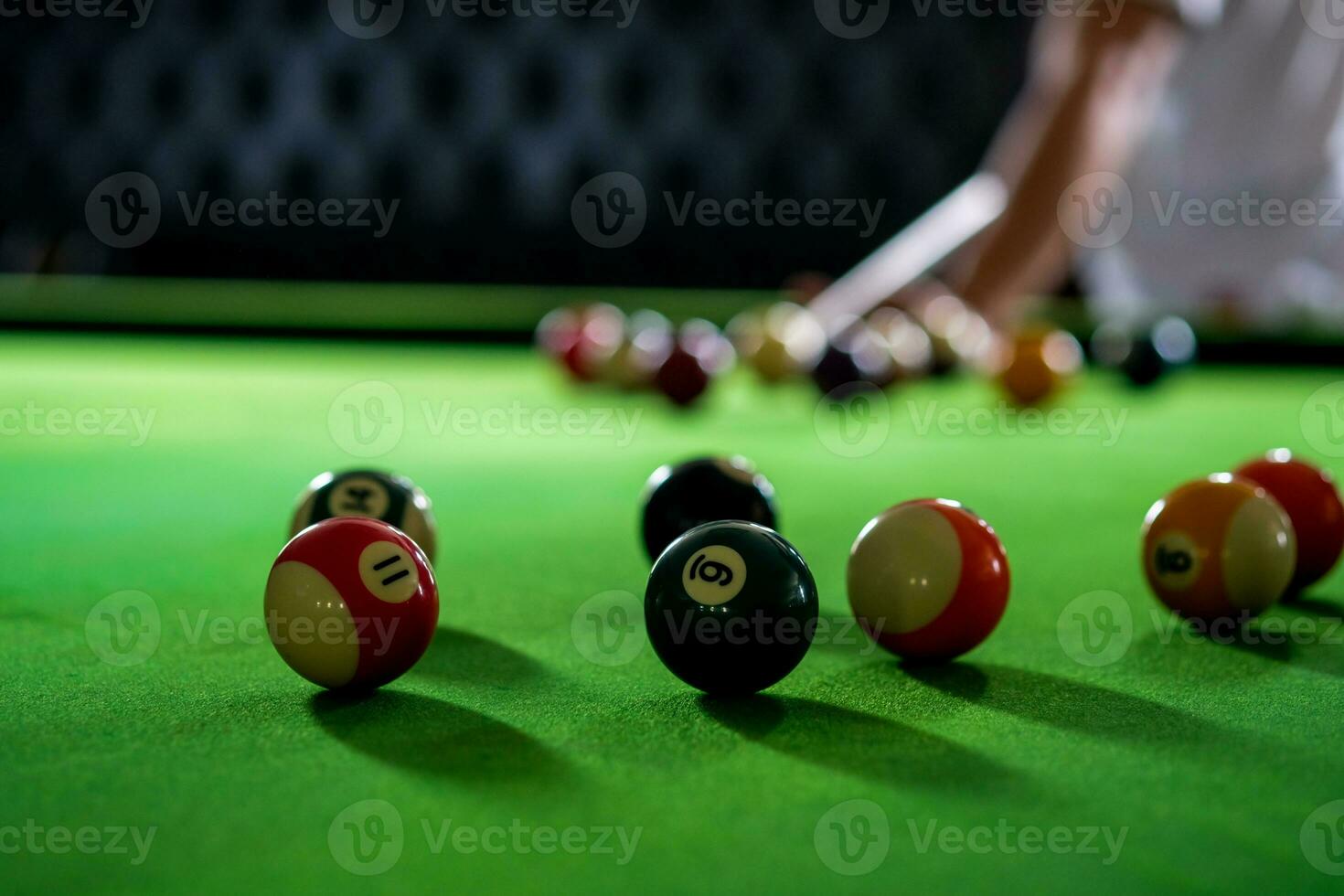 mannens hand och kö ärm spelar snooker spel eller framställning siktar till skjuta slå samman bollar på en grön biljard tabell. färgrik snooker bollar på grön fris. foto