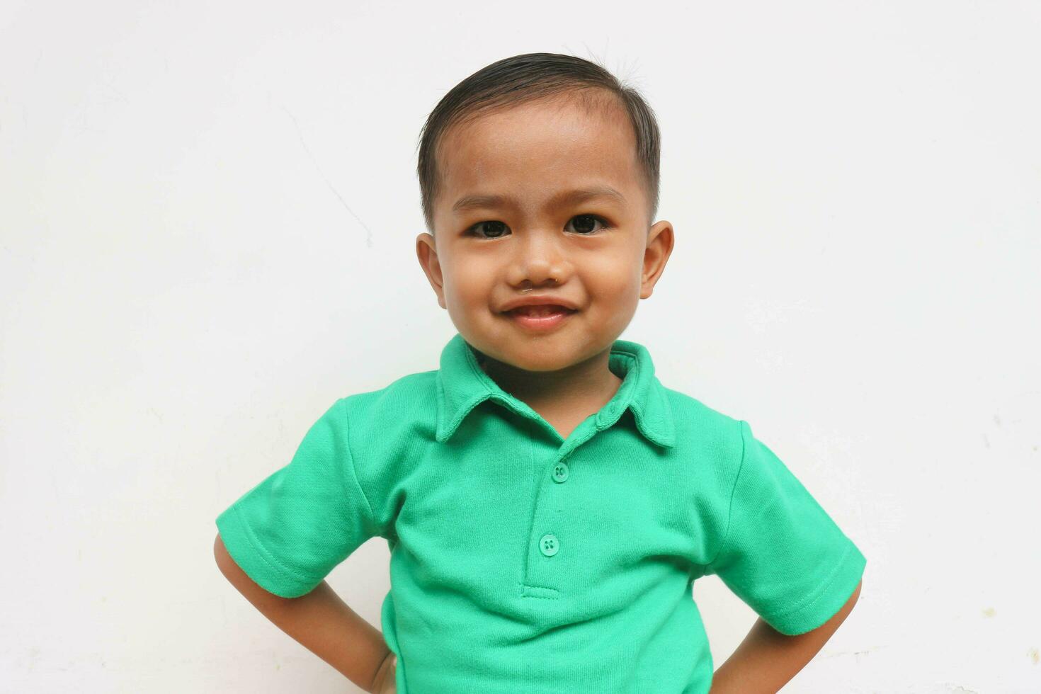 porträtt av en söt liten asiatisk pojke stående och leende medan ser på kamera, på de vit bakgrund foto