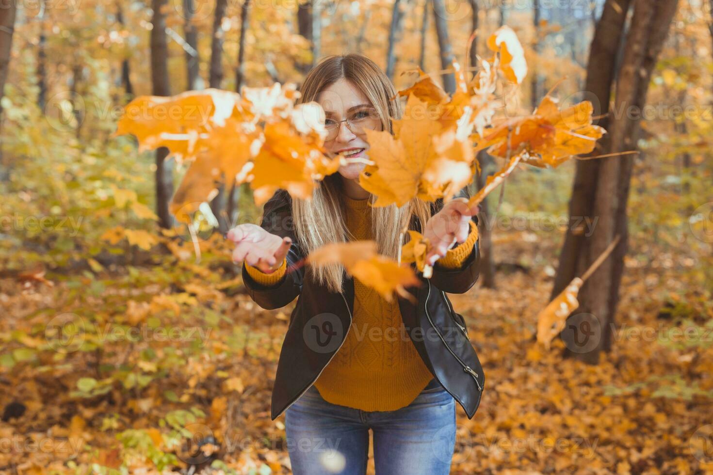 Lycklig skrattande ung kvinna kasta löv i höst parkera. falla säsong foto