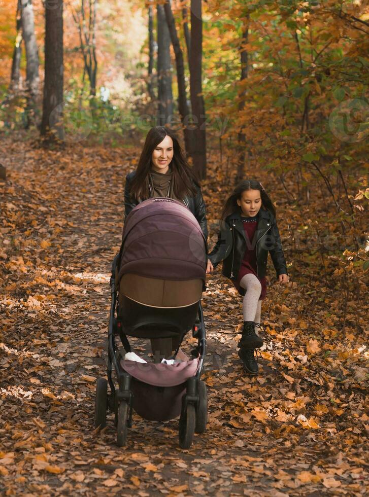 mor och henne liten dotter och en bebis i pråm på promenad i höst trä foto