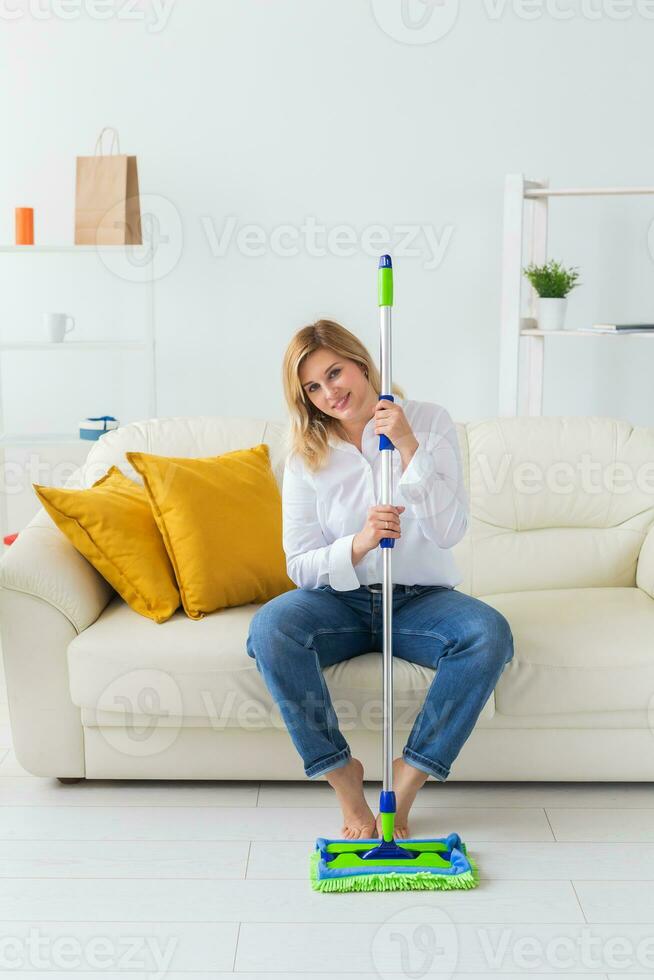 leende tusenåriga kvinna hemmafru med mopp för tvättar golv åtnjuter rengöring i minimalistisk interiör. hushåll rengöring tjänster och inhemsk arbete hushållning foto