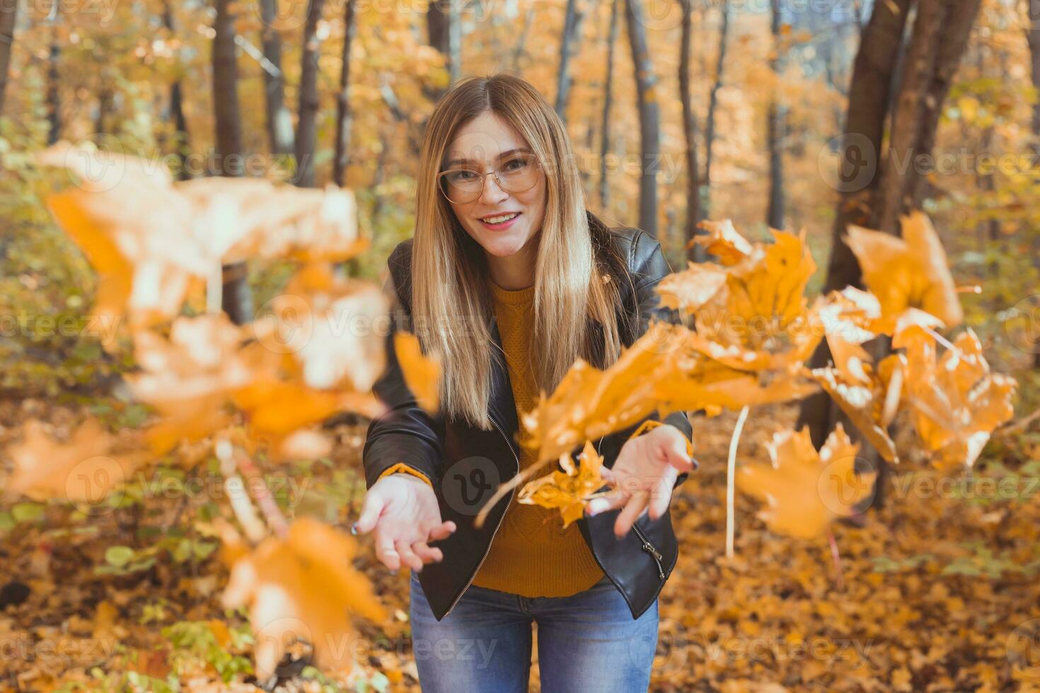 Lycklig skrattande ung kvinna kasta löv i höst parkera. falla säsong foto