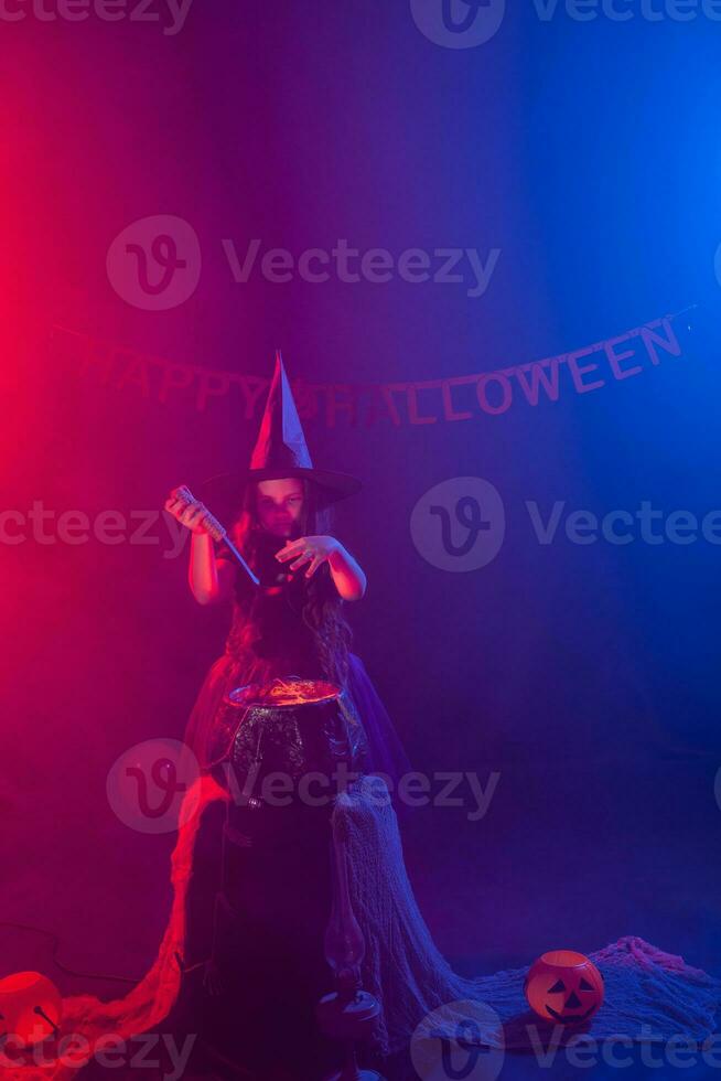 barn flicka häxa framställning en trolldryck i de kittel på halloween högtider. foto