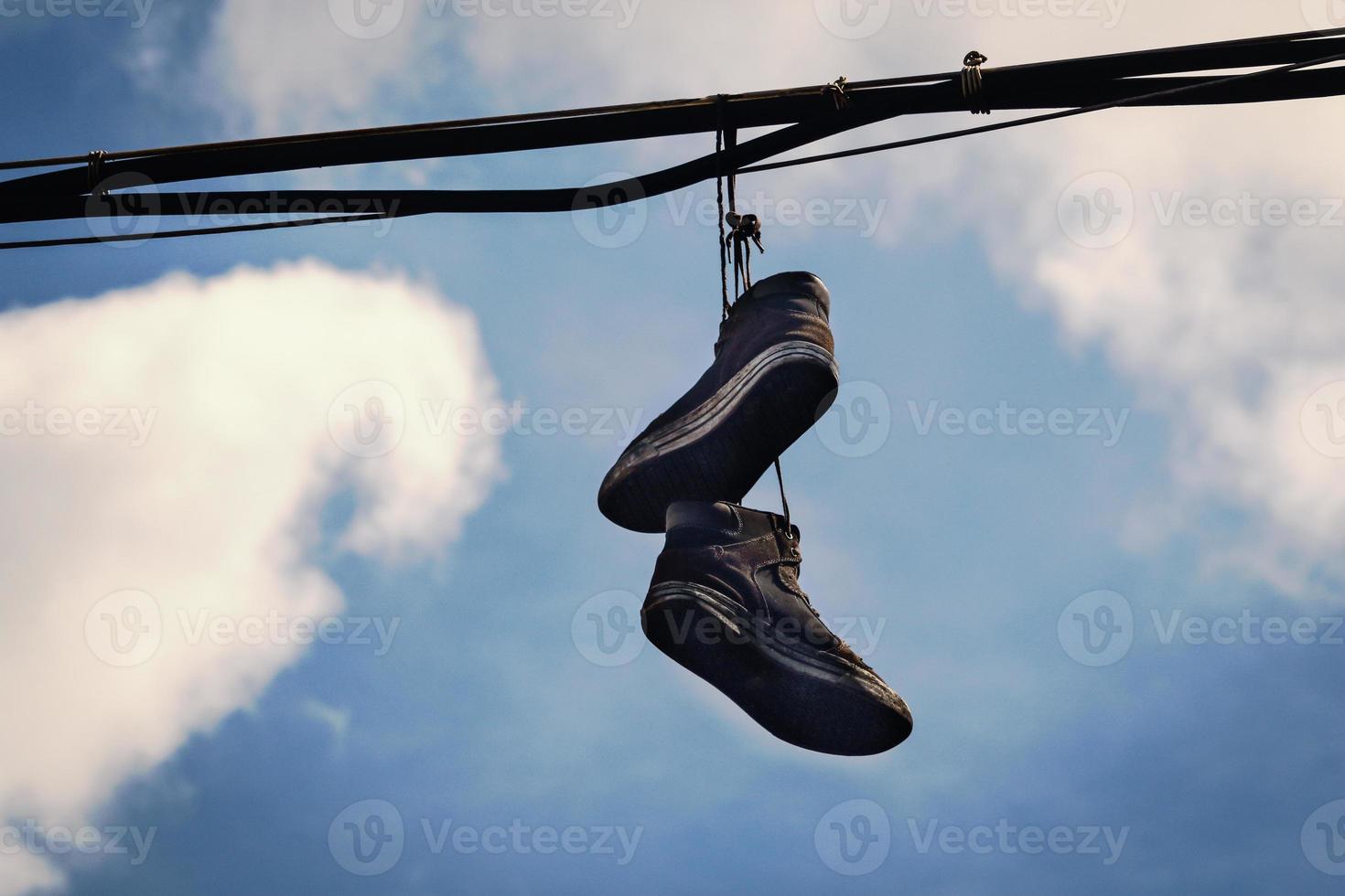 två smutsiga gamla sneakers som hänger på ledningar i blå himmel med moln foto