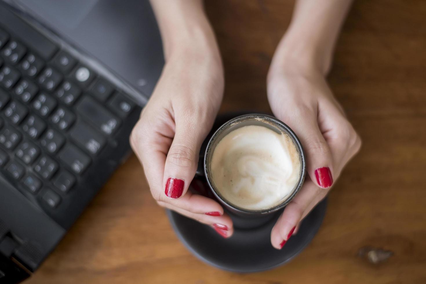 kvinna som håller varm cappuccino på skrivbordet foto