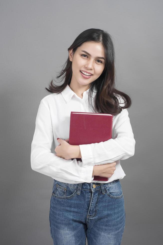 porträtt av kvinnahögskolestudentinnehavbok i studiogrå bakgrund foto