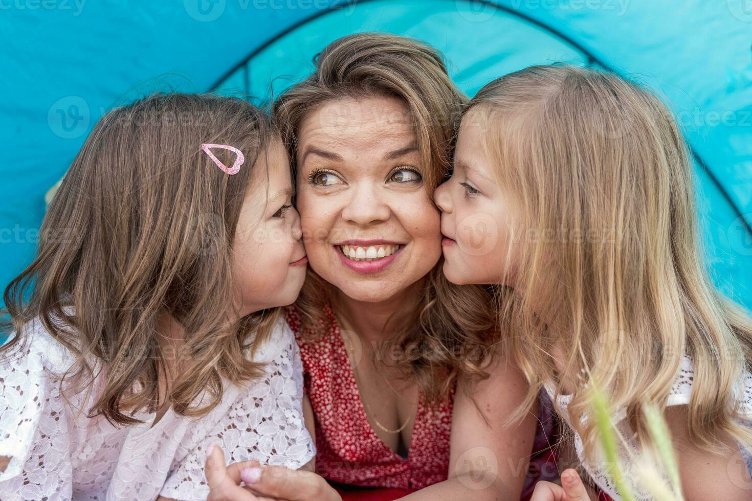 porträtt av söt blond mamma med henne döttrar liggande ner i en blå camping tält foto