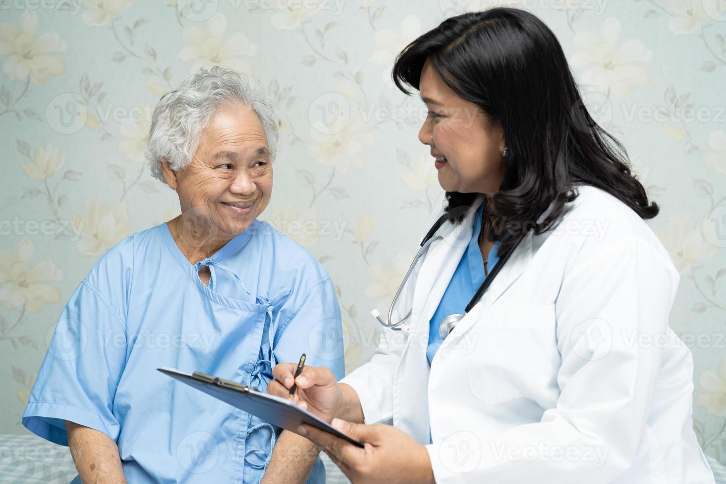 läkare som talar om diagnos och anmärkning på Urklipp med asiatisk senior eller äldre gammal damkvinna medan du ligger på sängen på vårdavdelningen, hälsosamt starkt medicinskt koncept. foto