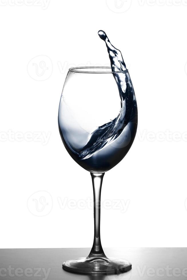 ett stänk av vatten i ett glas vinglas. vattenstänk i glas på glödande bakgrund. transparent vätska som stänker i vinglas. mat, objekt. foto