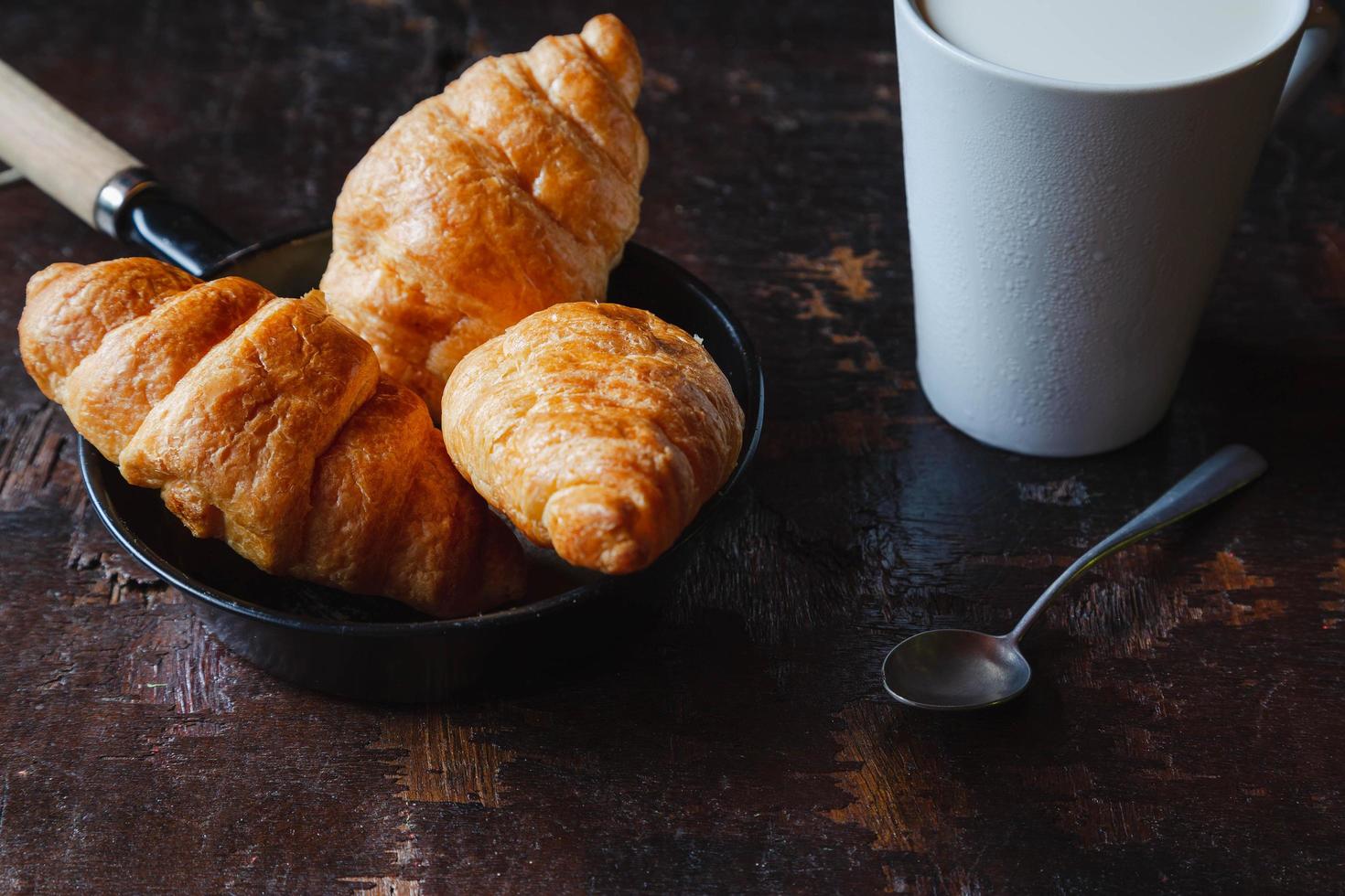 frukostbröd, croissanter och färsk mjölk på träbordet. foto