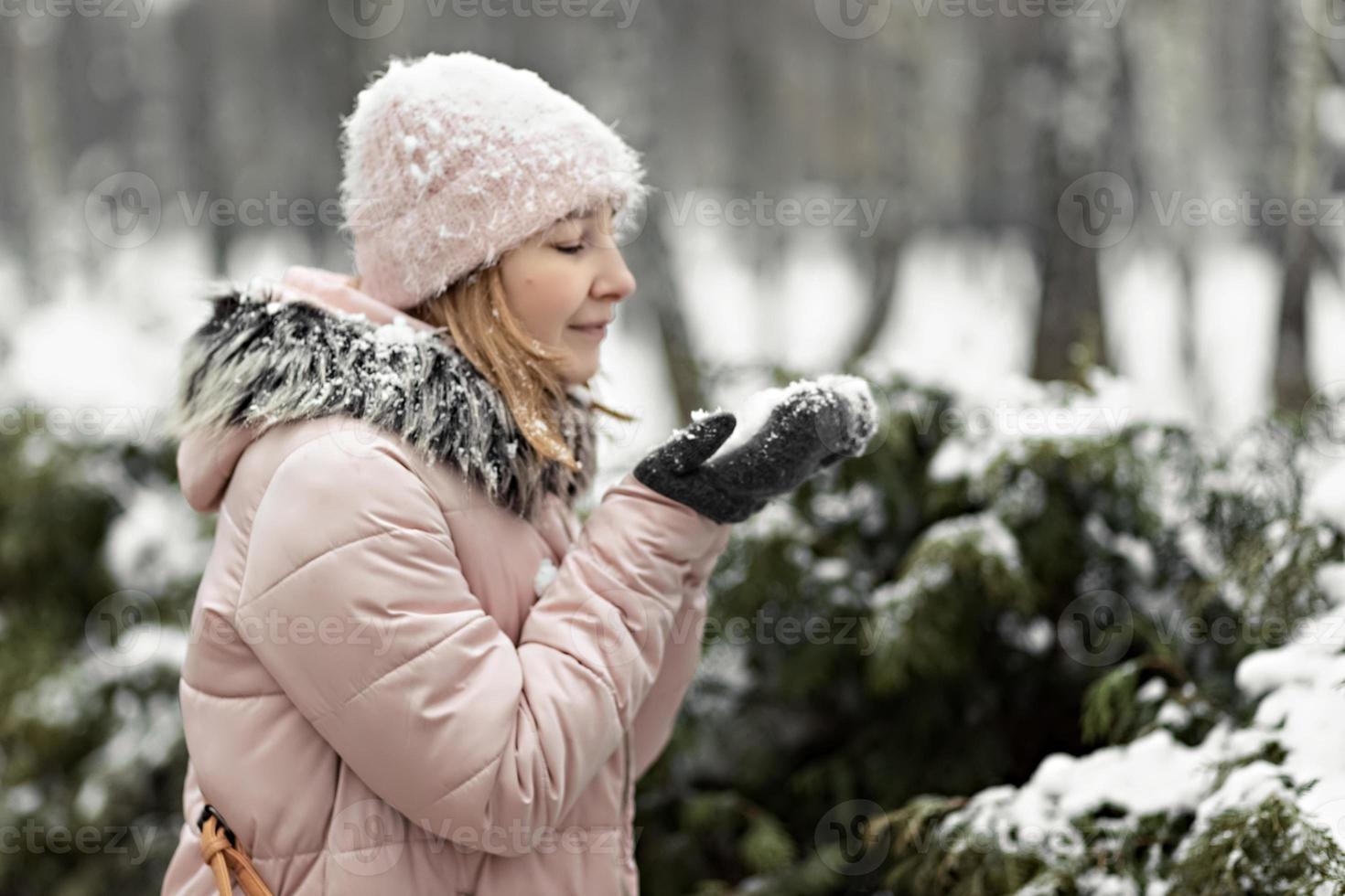 glad kvinna på en snöig vinterdag i parken, klädd i varma kläder, blåser snön av sina vantar foto