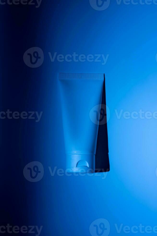 attrapp av vit pressa flaska plast rör för branding av medicin eller kosmetika - grädde, gel, hud vård, tandkräm. kosmetisk flaska behållare på en blå neon bakgrund. minimalism foto