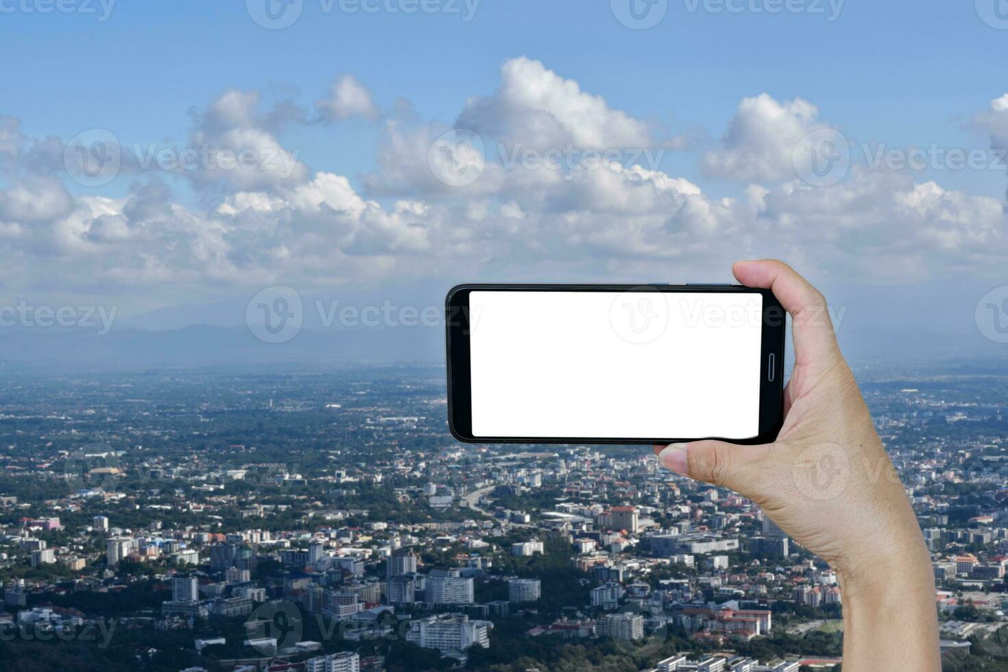hand innehav smartphone tom skärm över blå himmel moln och stad. foto