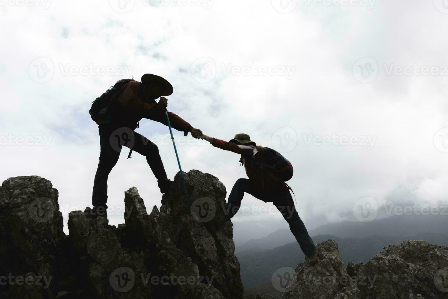 silhuett av två manlig vandrare klättrande upp berg klippa och ett av dem ger portion hand. människor portion och, team arbete begrepp. foto