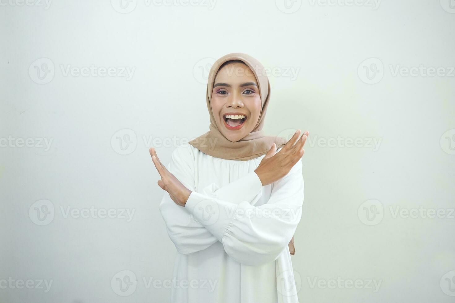 Lycklig ung asiatisk muslim kvinna korsning händer gör sluta gest och demonstrerar avslag isolerat över vit bakgrund foto