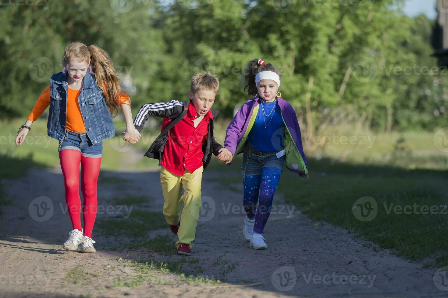 glad barn en pojke och två flickor i Häftigt klädespersedlar springa längs de väg foto