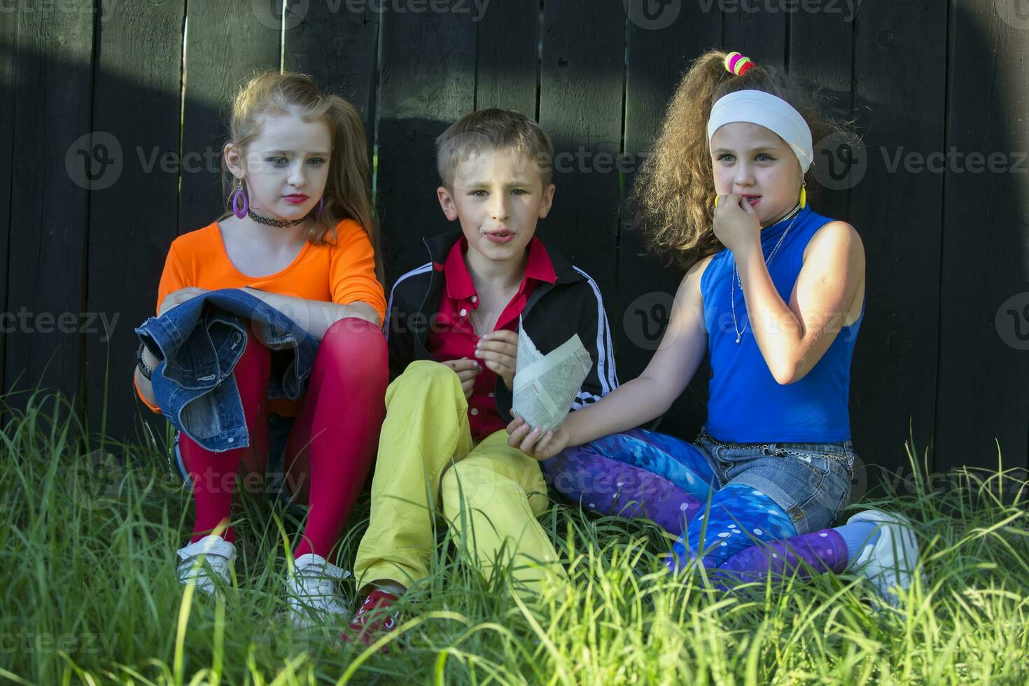skön modell barn i ljus kläder sitta på de gräs nära en trä- staket. foto