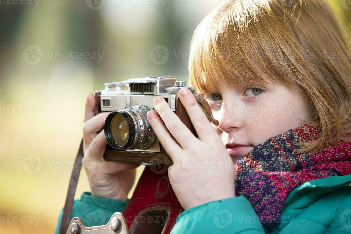 liten rödhårig flicka med en retro kamera i de höst parkera. barn fotograf. foto