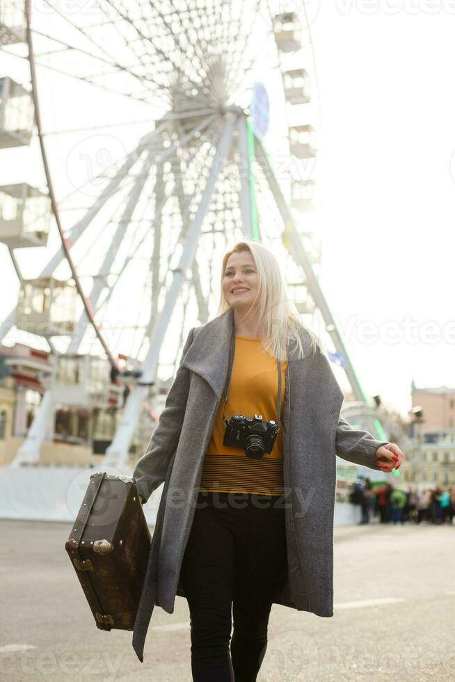 ung kvinna gående utomhus på de stad gata nära ferris hjul leende glad. foto