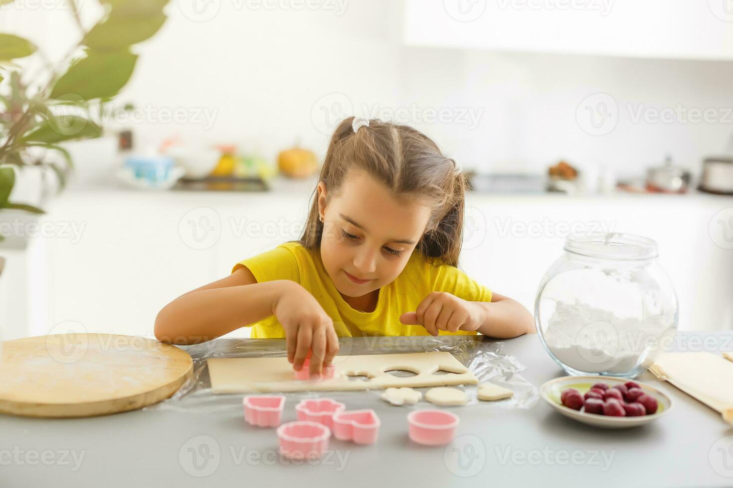 liten flicka gör småkakor från de deg i de kök på Hem foto