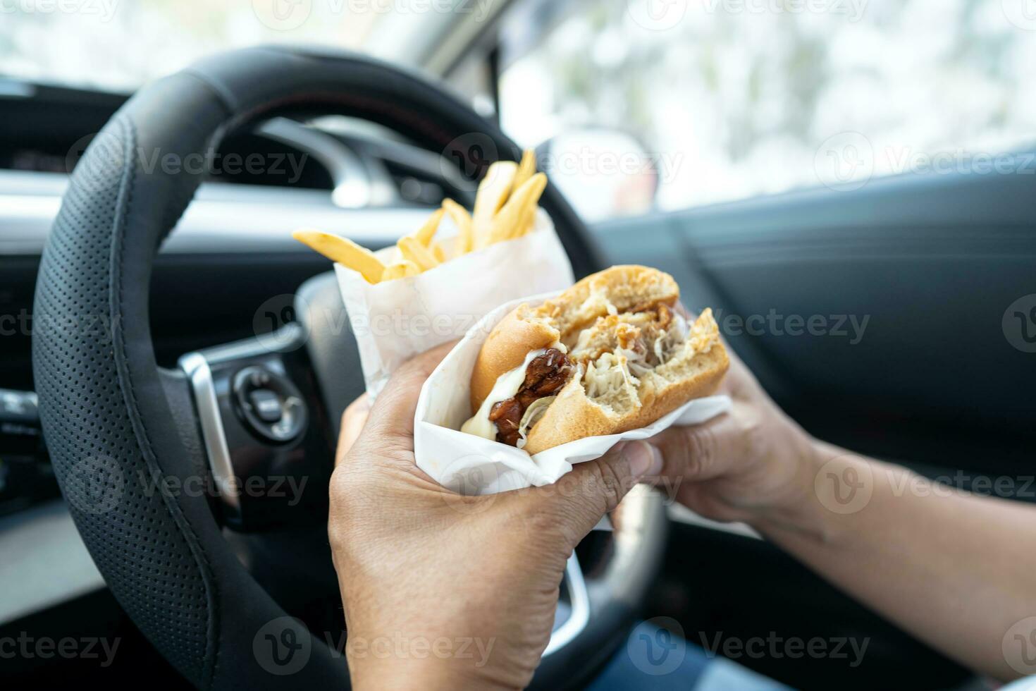 asiatisk lady innehav hamburgare och franska frites till äta i bil, farlig och risk ett olycka. foto