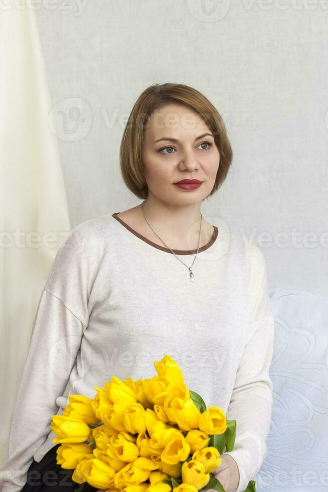 porträtt av en ung skön flicka. en flicka och en stor bukett av färsk gul tulpaner. de begrepp av vår och Semester, Mars 8, internationell kvinnors dag, foto