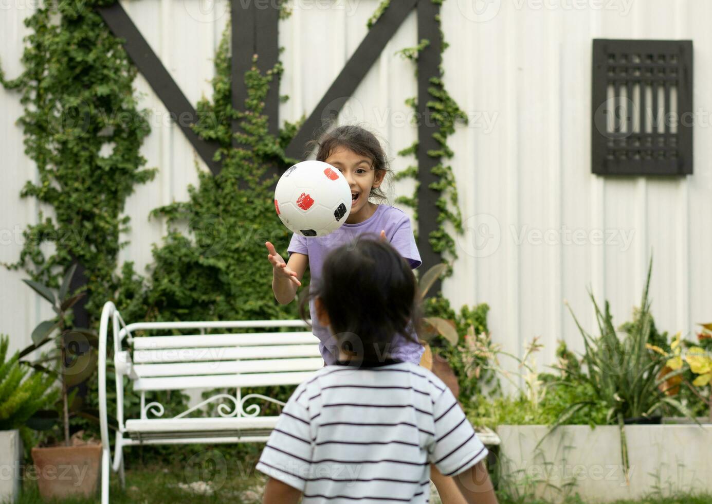 rolig liten pojke och flicka spelar boll i trädgård foto