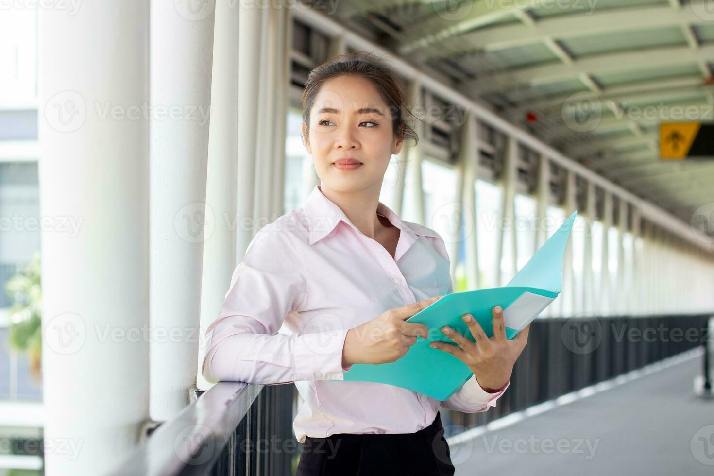 skön asiatisk kvinna i kostym innehav mapp på korridor. foto