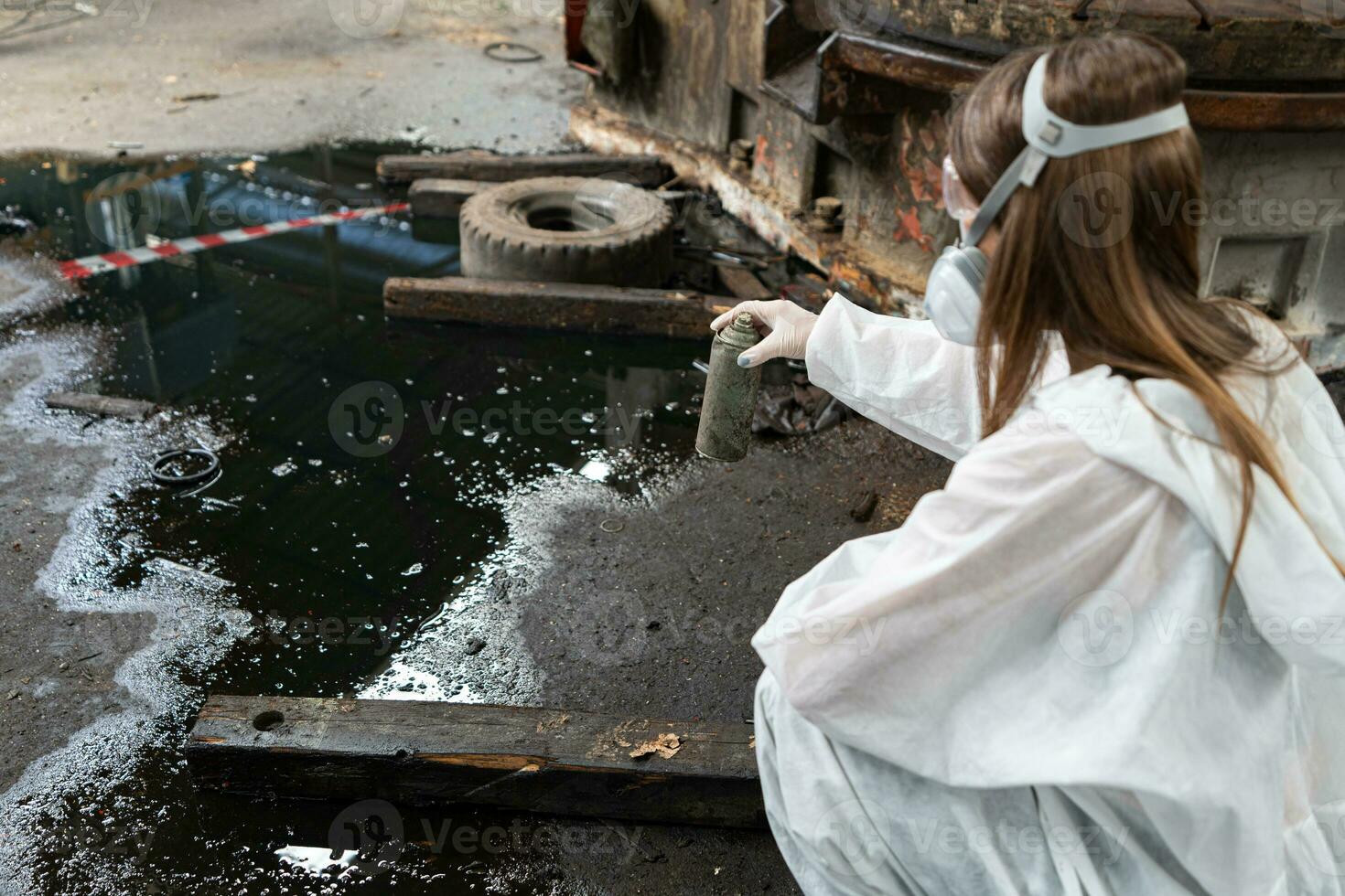 nödsituation förorening fabrik begrepp. kvinna kemist bär ppe och gas mask inspekterande olja på fabrik golv foto