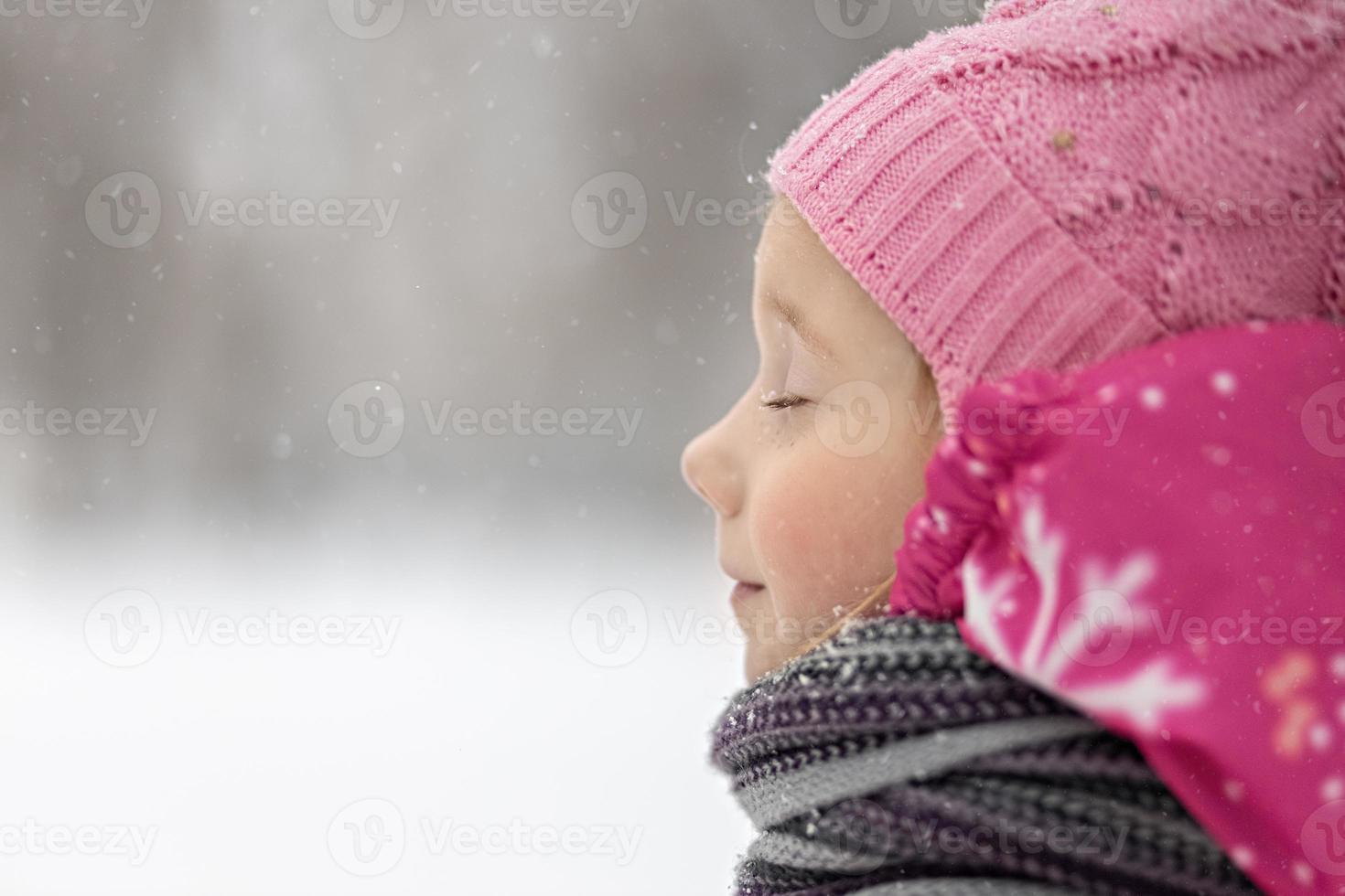 porträtt av en liten flicka i rosa närbild. ett barn njuter av snöfallet. jullov foto