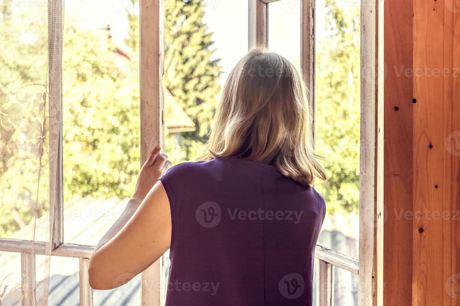 ung kvinna öppnar fönstret i sitt herrgård, tittar på trädgården foto