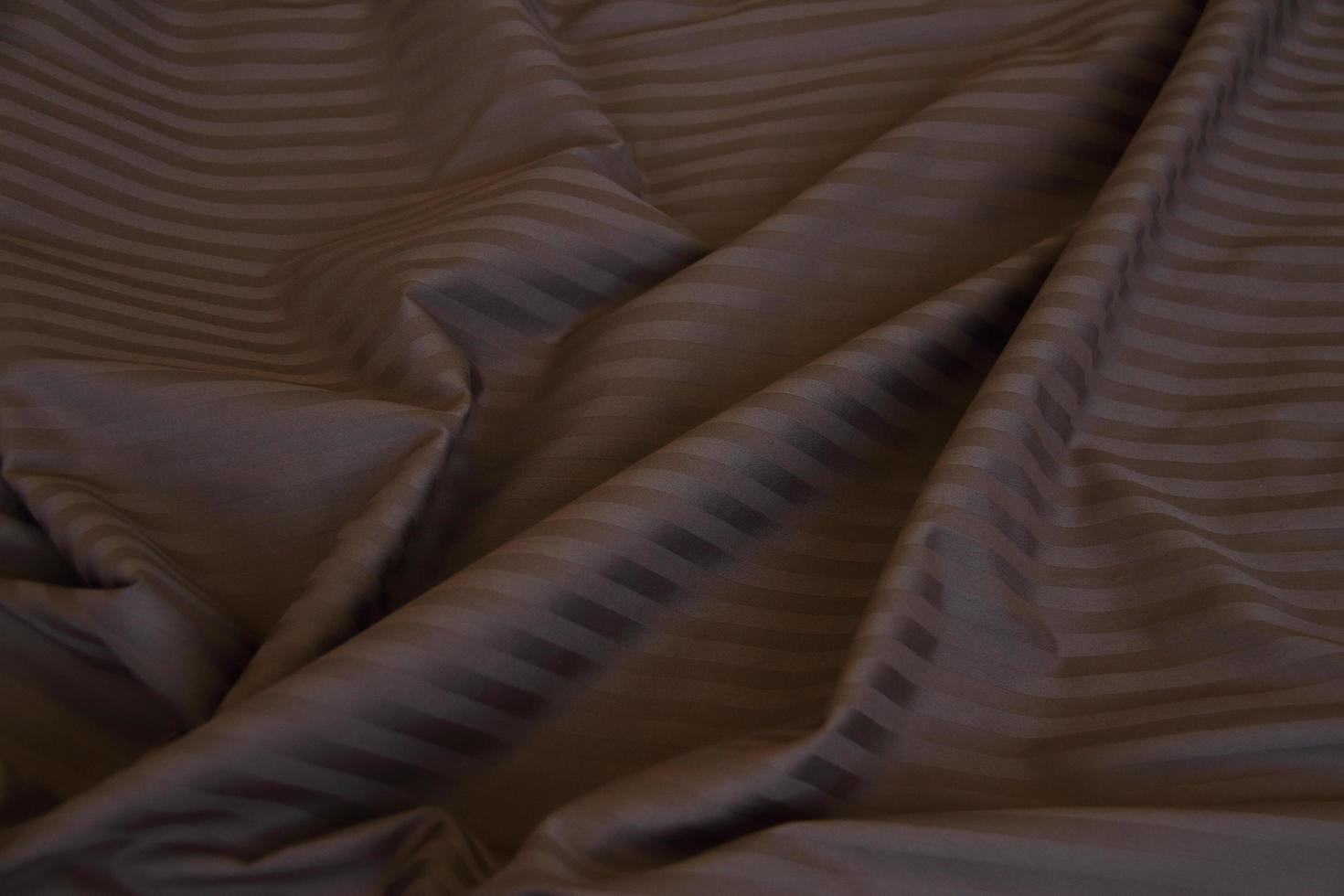 skrynkligt material med rynkor, veck på tyg, tygbakgrund. sängkläder. brun med ljusa ränder, tom foto