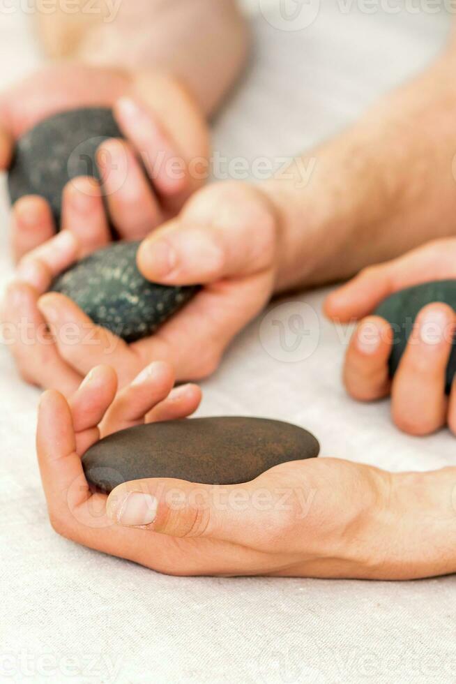 fyra händer av manlig massörer innehav spa stenar på vit handduk topp se. sten massage begrepp. foto