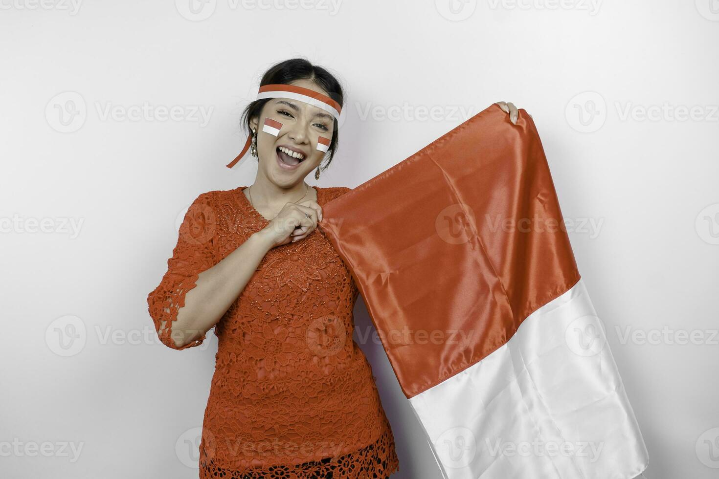 Lycklig leende indonesiska kvinna bär röd kebaya och pannband innehav Indonesiens flagga till fira indonesien oberoende dag isolerat över vit bakgrund. foto