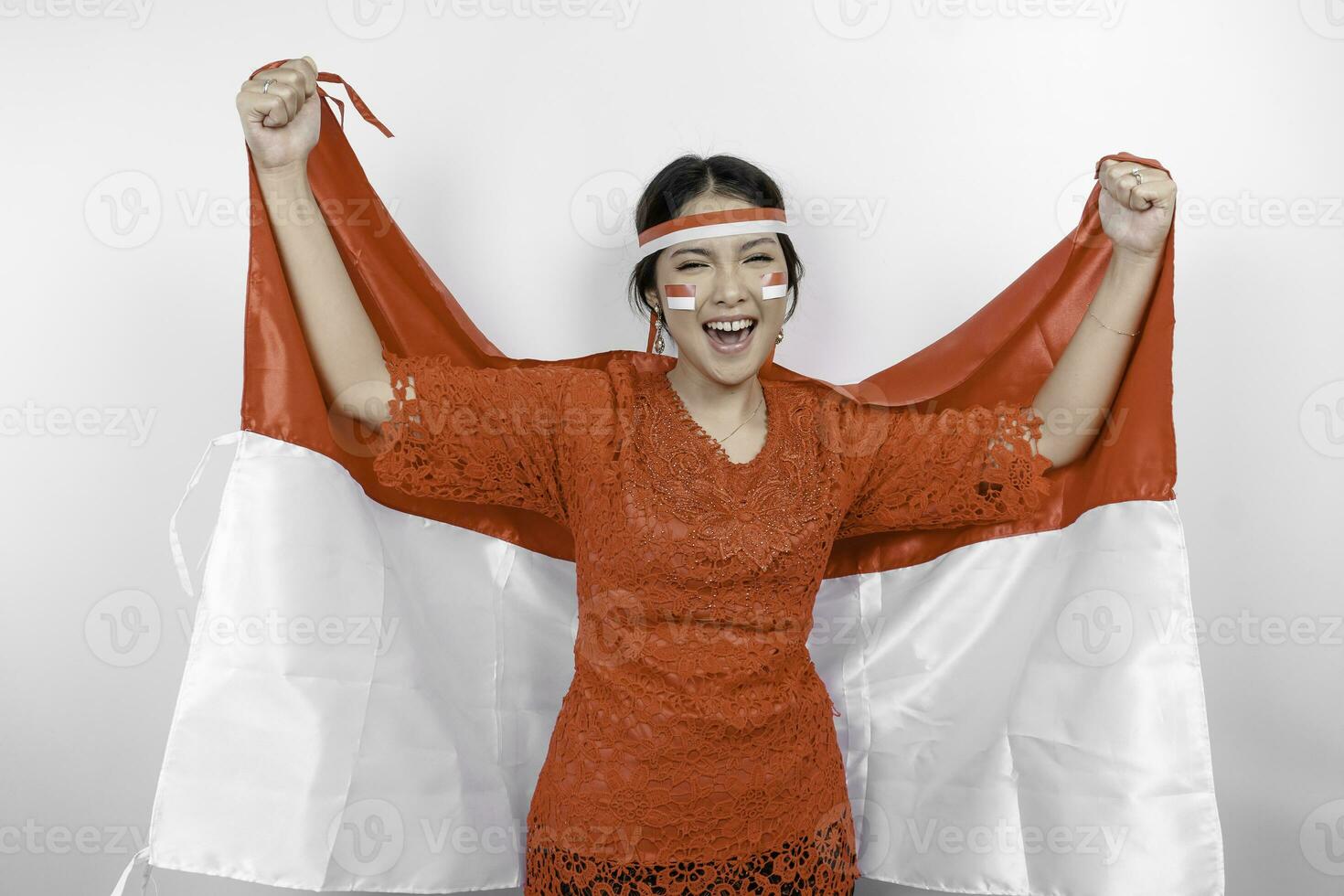 Lycklig leende indonesiska kvinna bär röd kebaya och pannband innehav Indonesiens flagga till fira indonesien oberoende dag isolerat över vit bakgrund. foto