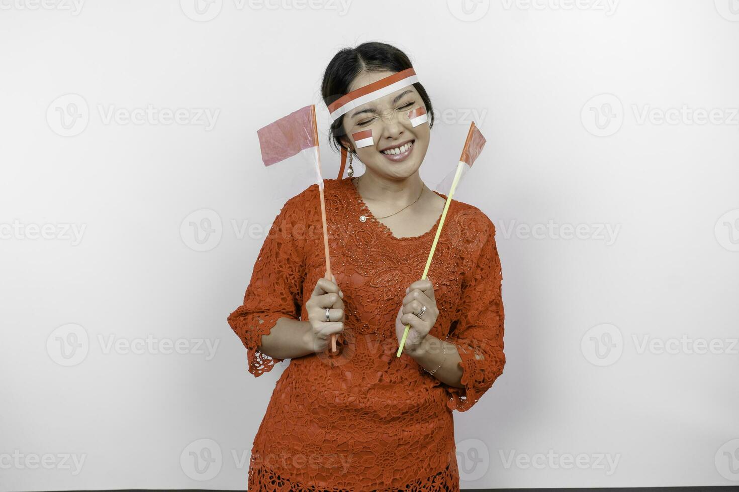 Lycklig leende indonesiska kvinna bär röd kebaya och pannband innehav Indonesiens flagga till fira indonesien oberoende dag isolerat över vit bakgrund. foto