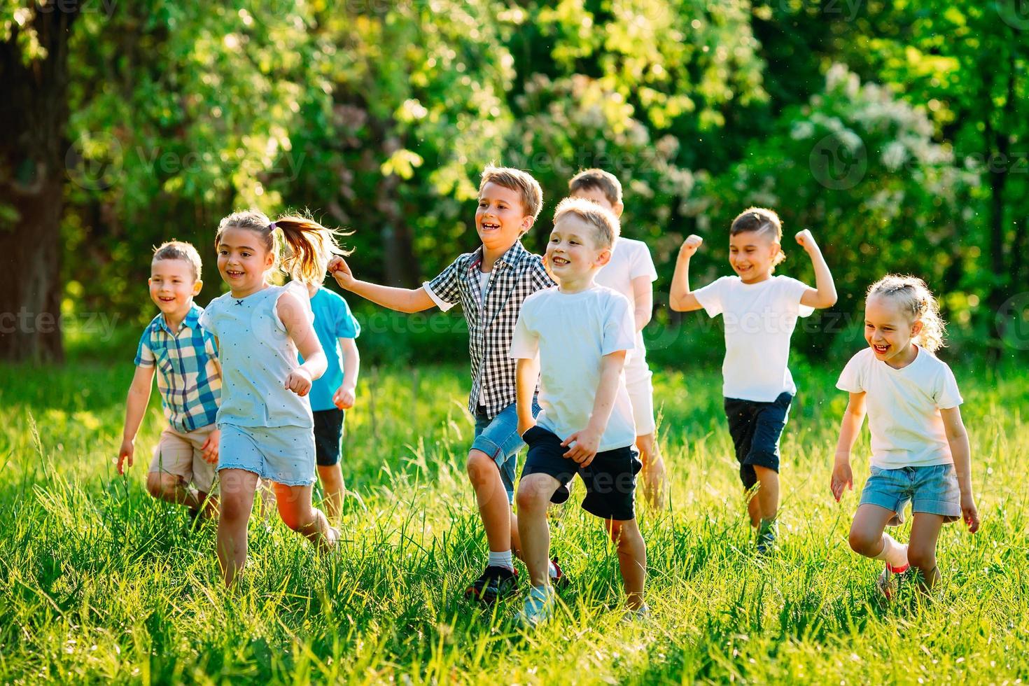 en grupp glada barn av pojkar och flickor springer i parken på gräset en solig sommardag. foto